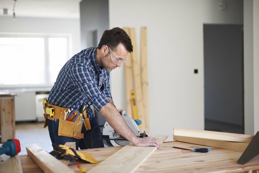 hausbau-haus-bauen-eigenleistung-handwerker-rohbau-03 Mann sägt Holz für den Innenausbau.